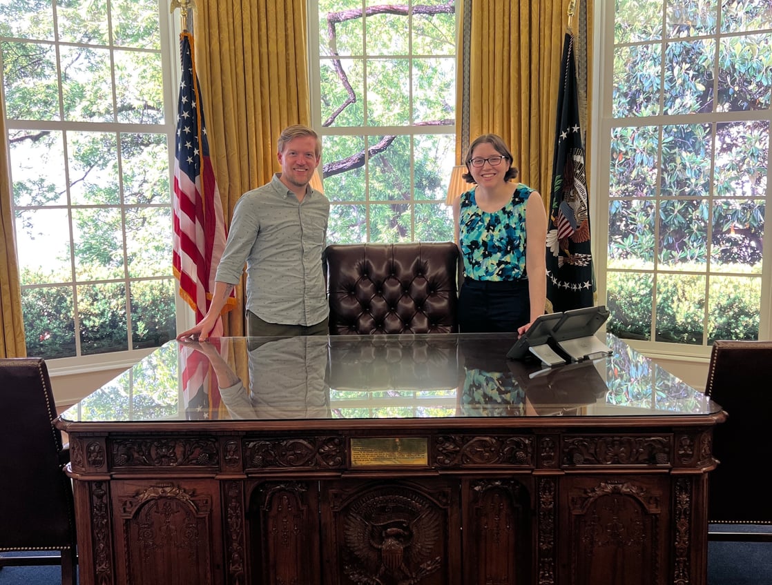 2 people at oval office desk with window